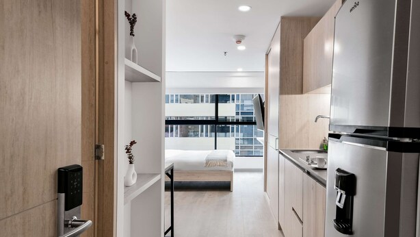 A modern kitchen with a built-in refrigerator, a coffee machine, and a view of a cityscape through large windows.