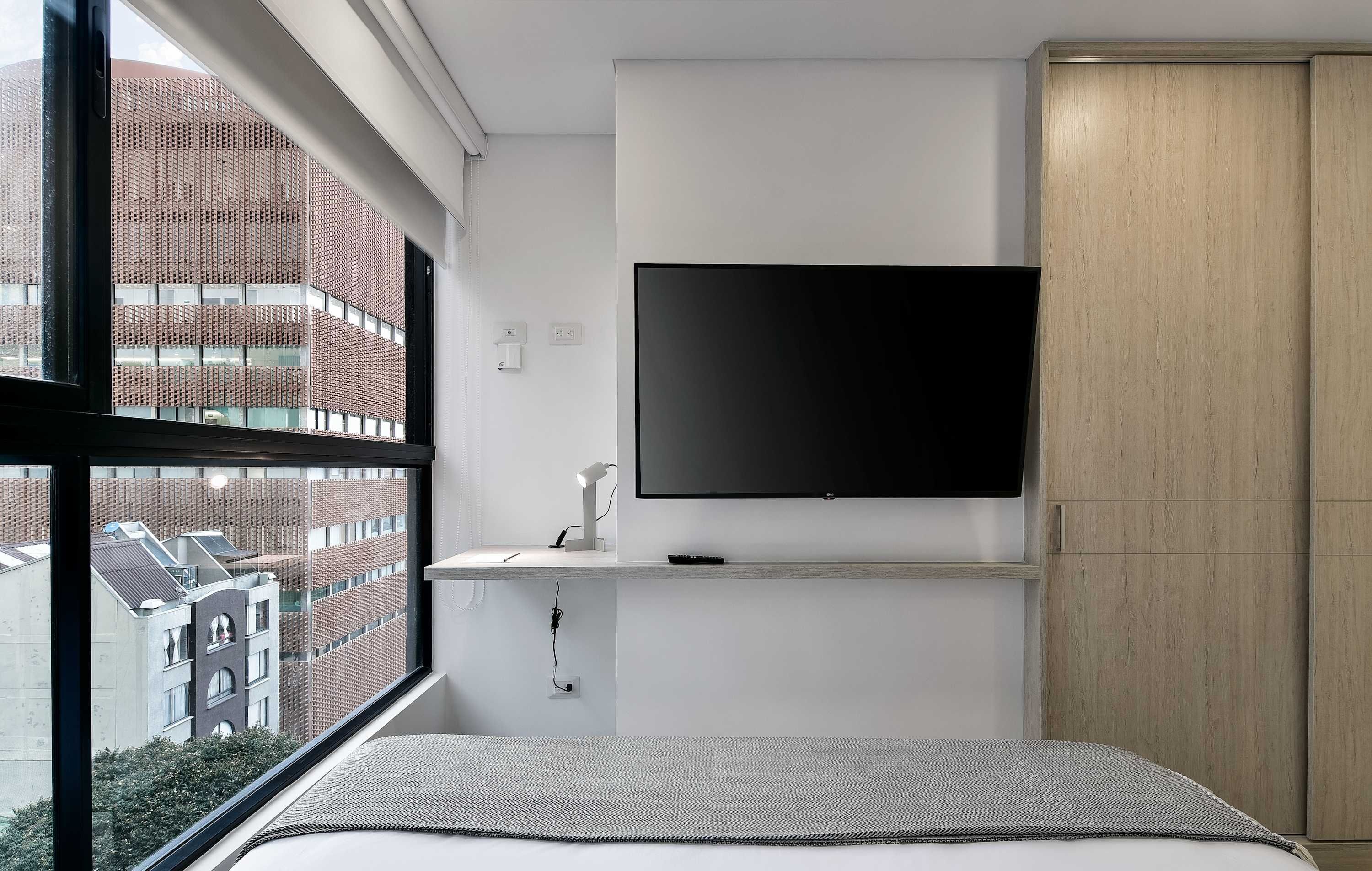 Un dormitorio moderno con un ventanal grande, un televisor de pantalla plana en la pared y un armario de madera.
