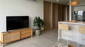 Ein modernes Wohnzimmer mit Flachbildfernseher, einem Topf mit Pflanze, einer Essecke mit Barhocker und einer Küche inklusive Kühlschrank.