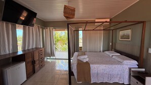 A bedroom with a four-poster bed, a wooden dresser, a television, and a balcony with curtains. - POUSADA O PORTUGA (São Miguel dos Milagres)