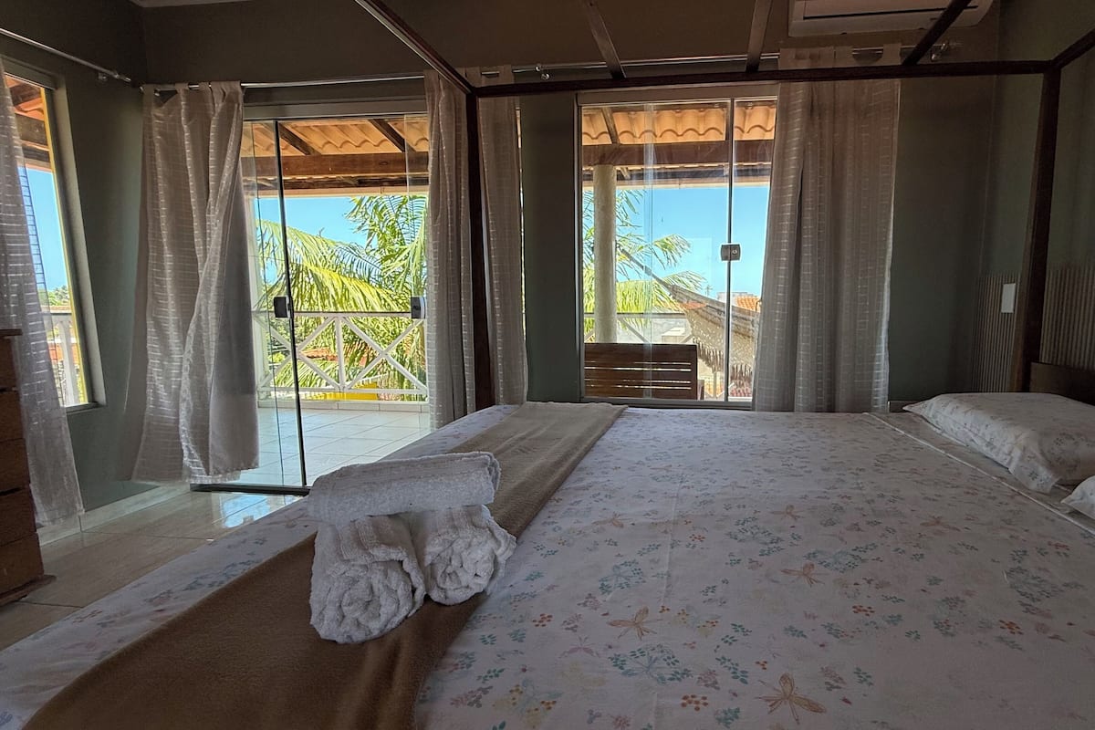 Ein Schlafzimmer mit einem großen Bett, Blick ins Freie und einem Fenster mit Vorhängen.