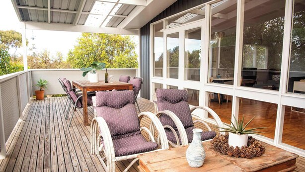 Eine Holzterrasse mit Korbmöbeln, einem Tisch und einem Blumentopf.