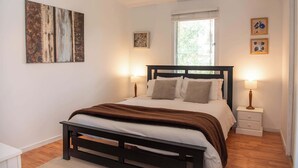 Ein Schlafzimmer mit einem Bett, Nachttischen, einem Fenster und Kunstwerken an den Wänden.