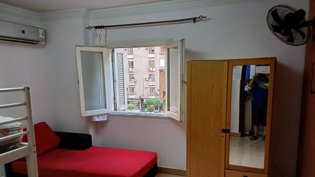 A room with a bed, a wardrobe, a window, and an air conditioning unit.
