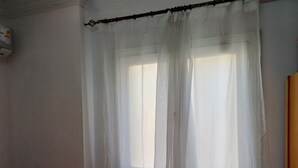 A room with a window covered by sheer white curtains, a white wall, and a partial view of a wooden door.