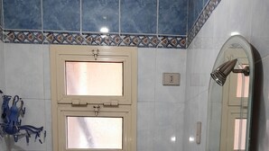 A bathroom with blue tiles, a white sink, a toilet, and a window with a decorative frame.