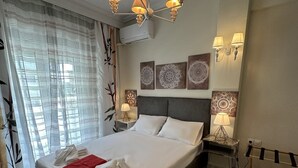 A hotel room with a large bed, a chandelier, wall-mounted lamps, and a window with curtains. - Allatini Sea View, Deluxe 2 Bedroom & Bathroom Apartment in Thessaloniki (Thessaloniki)