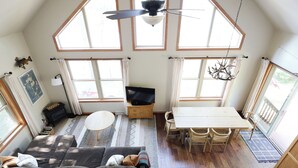 A spacious loft with a high ceiling, large windows, a dining area, and a cozy seating area.