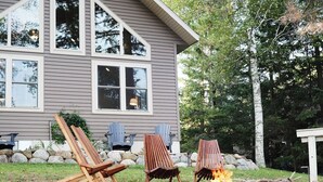 A house with a fire pit and two Adirondack chairs in the yard.