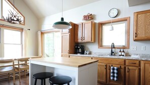 A kitchen with wooden cabinets, a large island with stools, a coffee machine, and a clock on the wall.