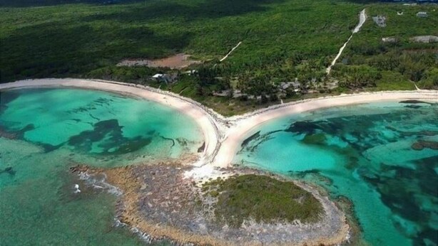 Luchtbeeld van een kustgebied met twee helderblauwe lagunes, een centrale weg en omliggend groen.