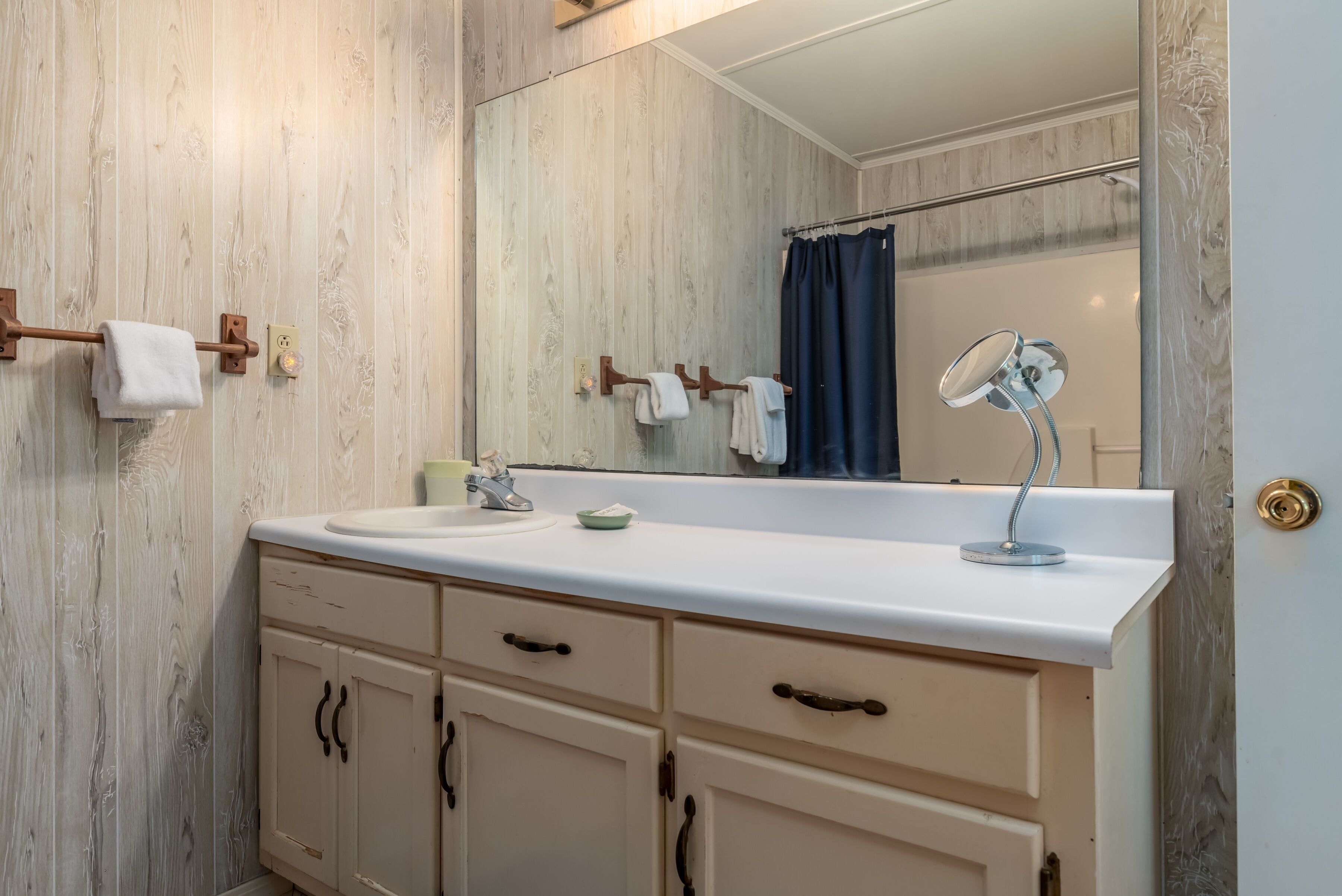 Un baño con pared de madera, un lavabo blanco, un espejo y un perchero para toallas.