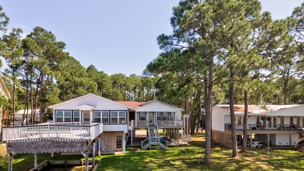 A waterfront property with two main buildings, a dock, and a small docked boat. - Happy Lee Ever After - 1424 Cadillac Avenue 2 Bedroom Home (Dauphin Island)
