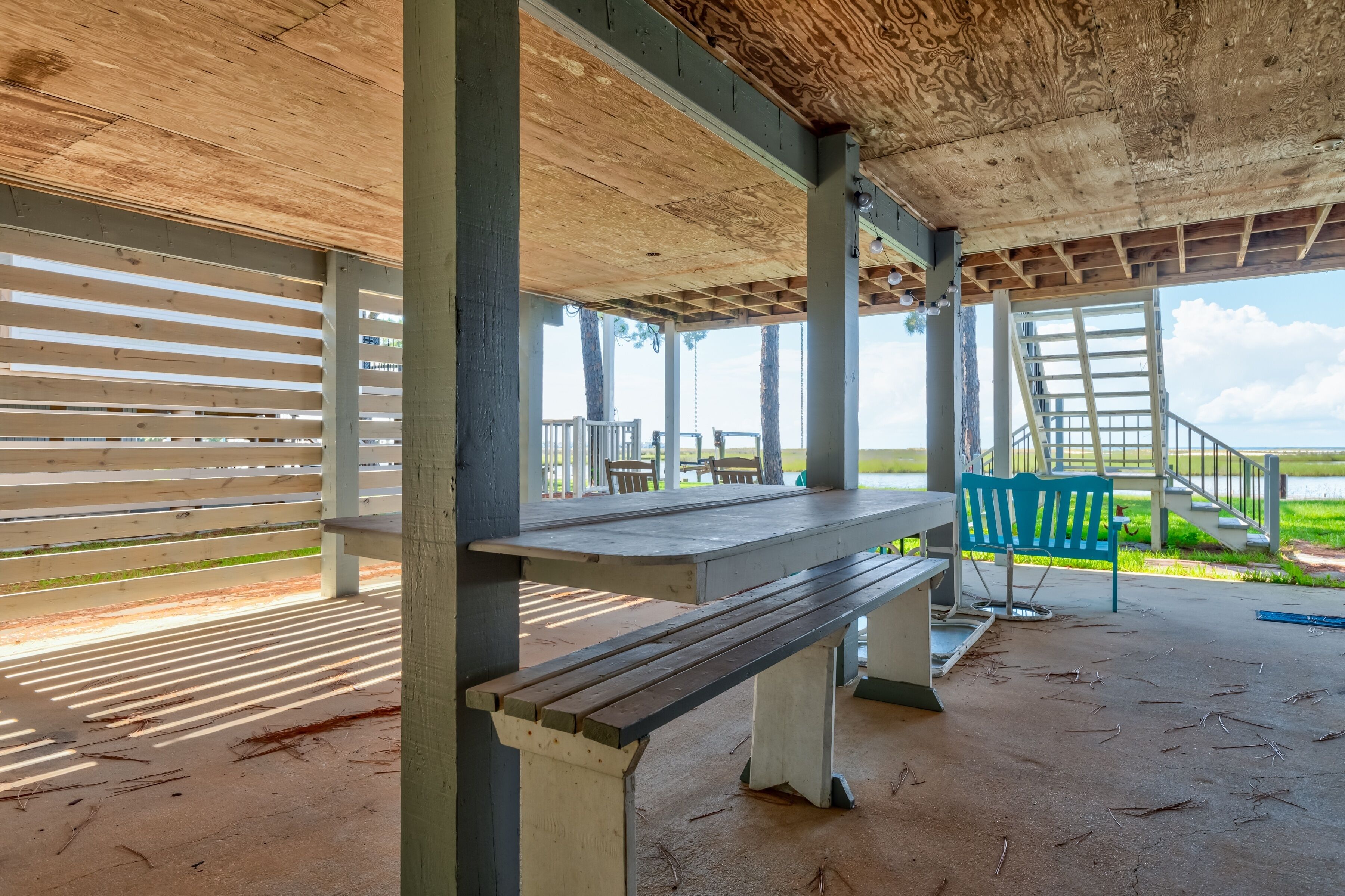 A covered outdoor area with a wooden bench, a table, and a staircase leading to an upper level.