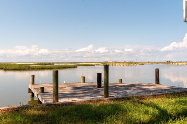A wooden dock extending into calm water with grassy banks and a clear sky.