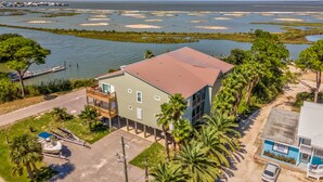A two-story building with a flat roof, a balcony, and a view of a water body with numerous small islands. - Bayou Heron #2b - 1514 Cadillac 2 Bedroom Condo (Dauphin Island)