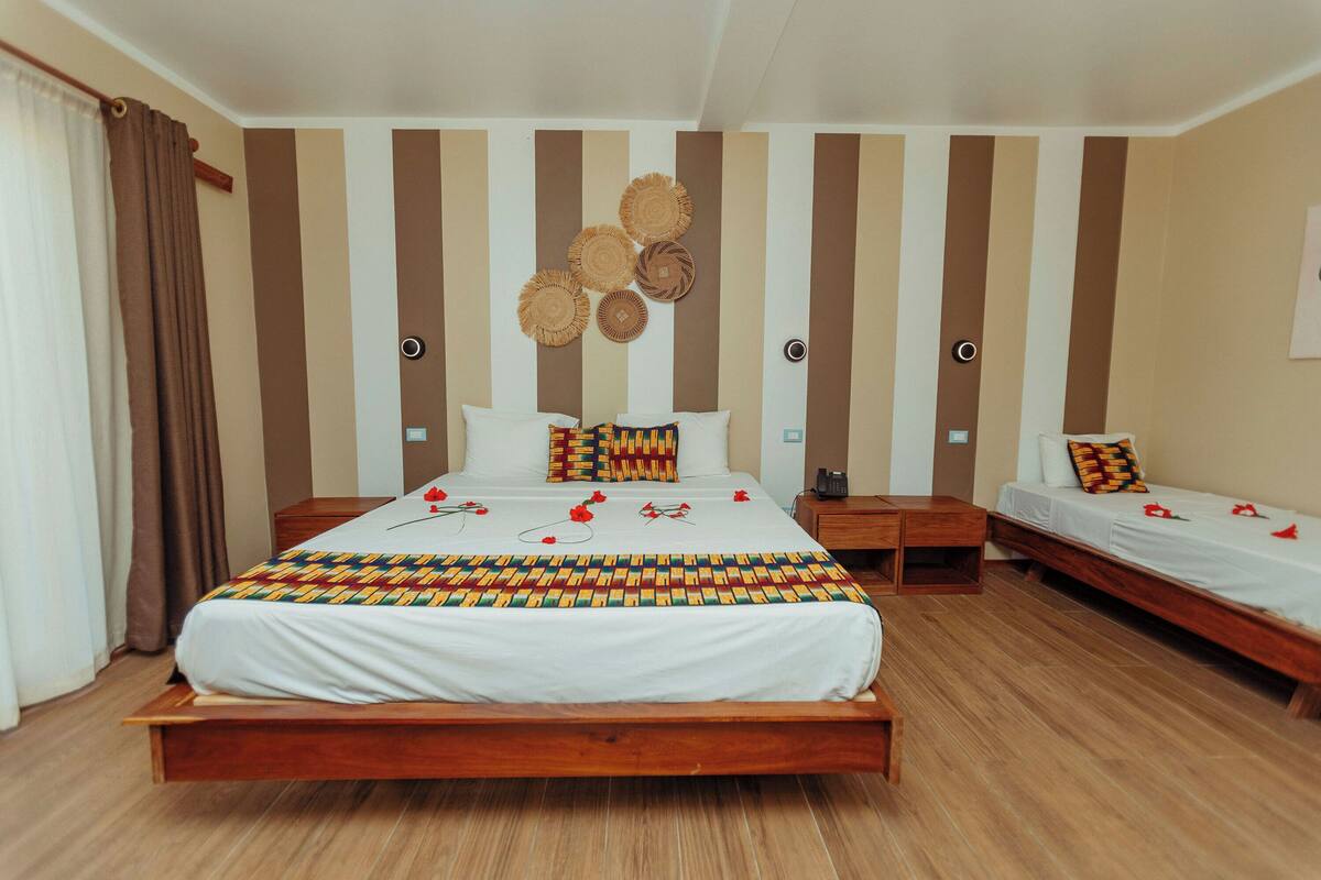 A hotel room with a large bed, a smaller bed, wooden flooring, and a striped wall design.