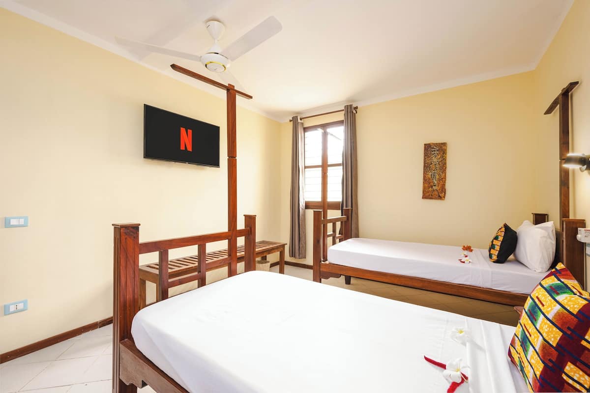 A room with two beds, a ceiling fan, a TV, and a window with curtains.
