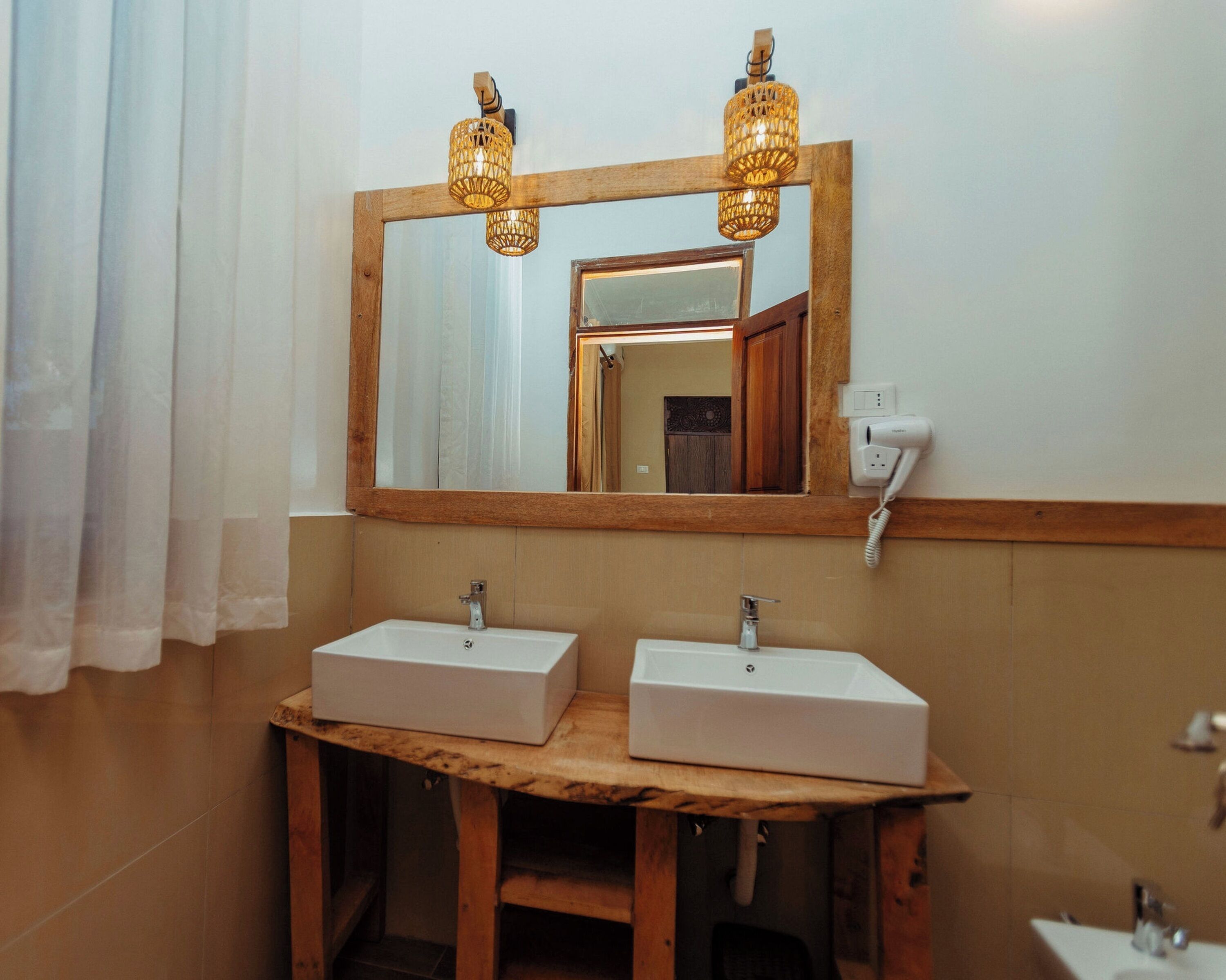 A bathroom with two sinks, a wooden vanity, a mirror with a wooden frame, and two wall-mounted light fixtures.