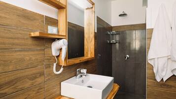 Un baño con lavamanos blanco, secador de pelo, ducha y paneles de pared de madera.