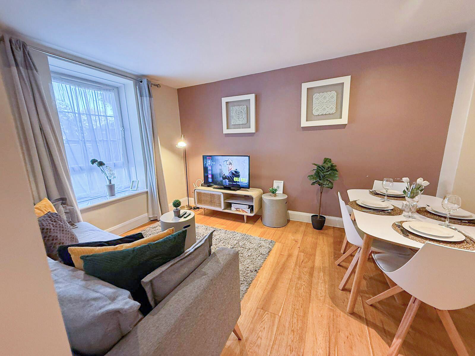 Una sala de estar moderna con sofá, televisor, juego de comedor y cuadros en la pared.