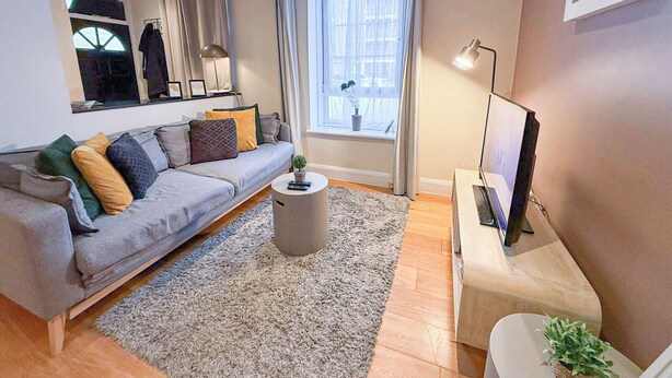 A modern living room with a grey sofa, a coffee table, a TV stand, and a window with curtains.