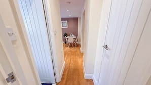 A hallway with wooden flooring and white walls, leading to a dining area with a table and chairs.