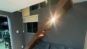 Een moderne woonkamer met een grijze bank, een trap en een groot raam.