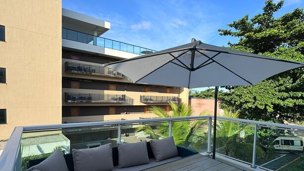 Een balkon met een bank, een tafel en een grote parasol.