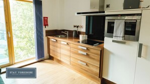 A modern kitchen with wooden cabinets, a built-in oven, and a large window with a view of trees. - 2nd Floor City Apartment (Sheffield)