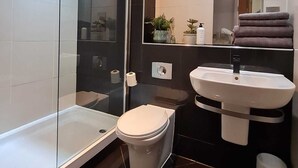A modern bathroom with a glass shower enclosure, a white toilet, and a white sink with a mirror above it. - 2nd Floor City Apartment (Sheffield)