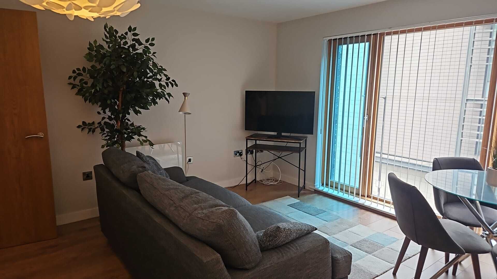 Una sala de estar con sofá, televisor y comedor con sillas.