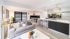 A modern living room with a grey sofa, a coffee table with a plant, and a dining area with a white table and chairs.
