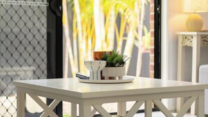 A white table with a basket, a potted plant, and a box labeled "excluido" in front of a glass door with a view of palm trees.