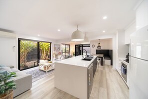 A modern kitchen with a central island, built-in appliances, and a dining area with a sofa and coffee table. - Hampton Holiday Home with Pool, BBQ & 10 min drive to Theme Parks! (Pimpama)