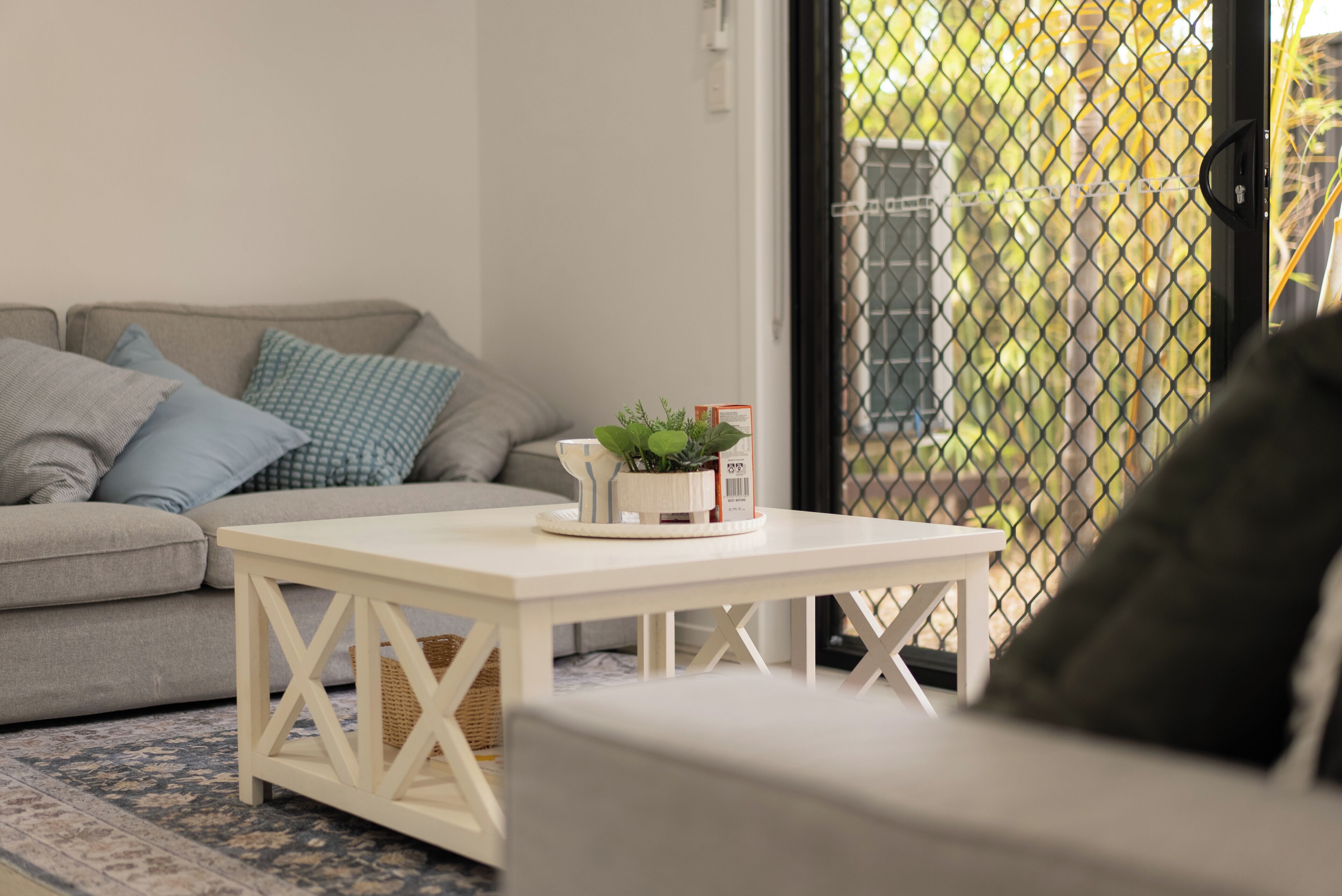 A living room with a white coffee table, a grey sofa, and a patterned rug.