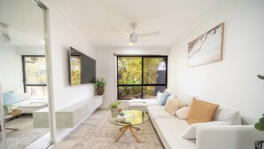 A modern living room with a white sofa, a glass coffee table, and a large window with a view of greenery.