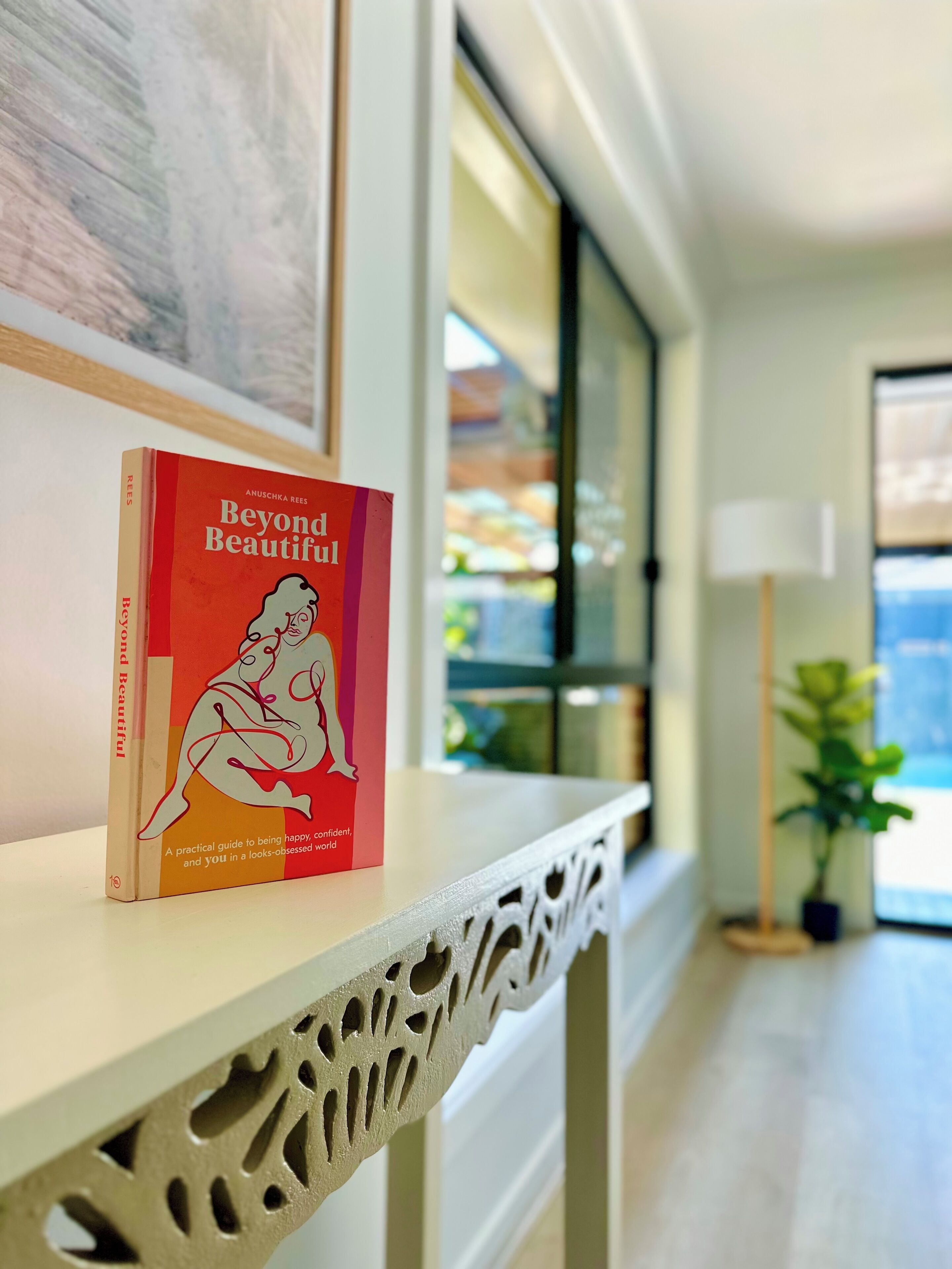 Un llibre anomenat 'Beyond Beautiful' sobre una estant blanca amb detall decoratiu.