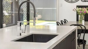 A modern kitchen with a stainless steel sink, a dining area with chairs, and a large wall clock.
