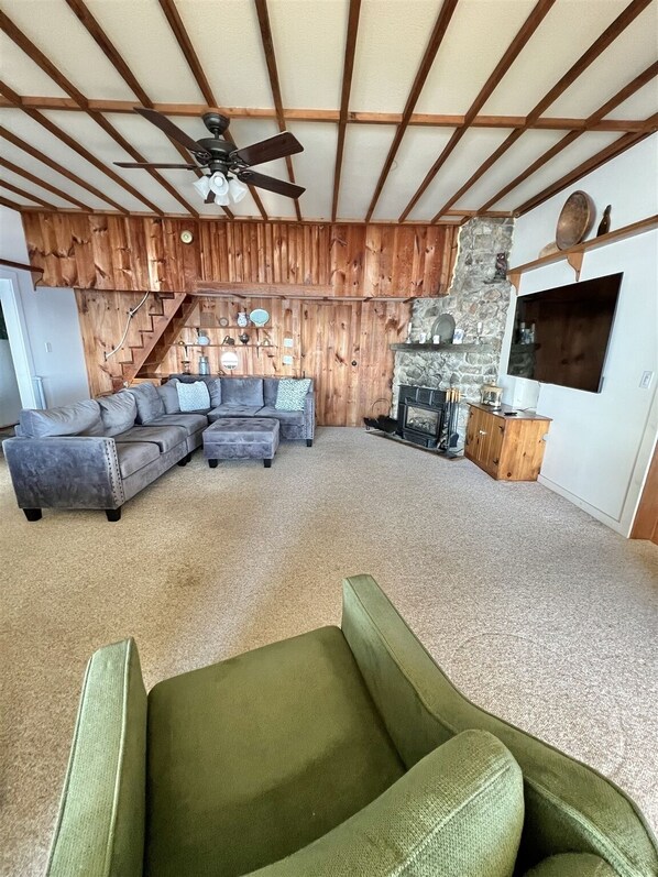 A cozy living room with a sectional sofa, a green armchair, a fireplace, and a stone wall.