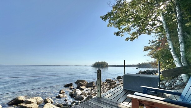 Une terrasse en bois offrant une vue sur un lac paisible, avec un barbecue et un banc.