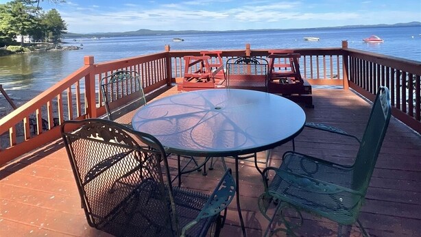 Een terras met een glazen tafel en metalen stoelen, met uitzicht op een waterpartij en verafgelegen land.