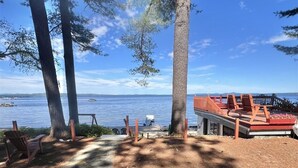 Een terras met houten stoelen en een tafel, met uitzicht op een waterpartij, omringd door bomen.