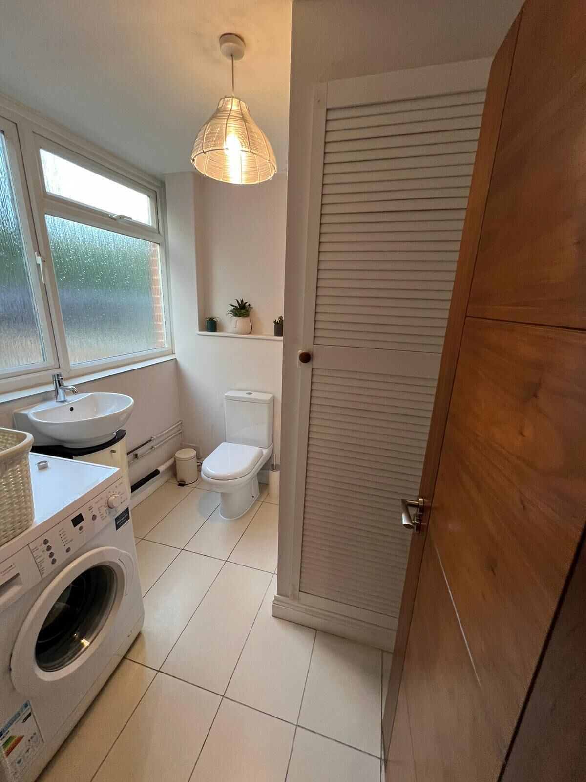A compact bathroom with a washing machine, sink, toilet, and a wooden wardrobe.