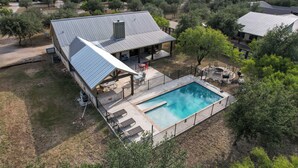 A modern house with a swimming pool, covered patio, and a view of surrounding trees and hills. - Large spacious home with wheelchair accessible pool (Concan)