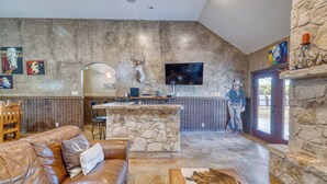 A rustic interior with a stone wall, a leather couch, a wooden dining table, and a mounted deer head. - Large spacious home with wheelchair accessible pool (Concan)