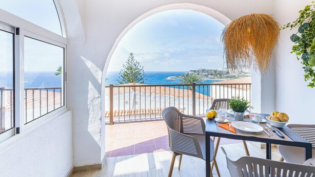 A balcony with a table set for breakfast, overlooking a coastal view.