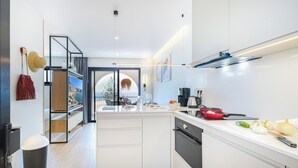 A modern kitchen with white cabinetry, a built-in oven, a coffee maker, and a view through a glass door to a balcony.
