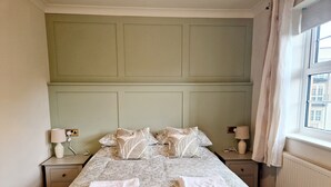 Una cama bien tendida con ropa de cama de estampado floral, dos lámparas de noche y una ventana con cortinas.