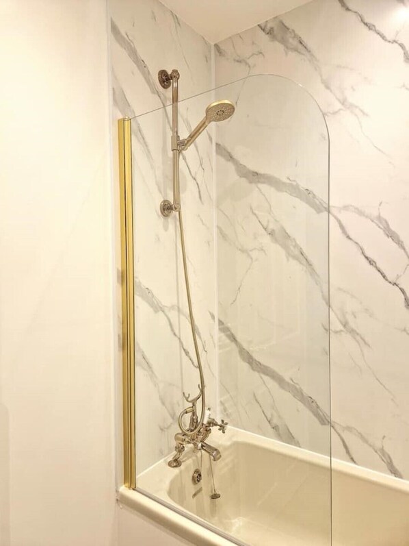 A bathroom with a marble wall, a bathtub, and a shower with a gold-colored showerhead and hose.